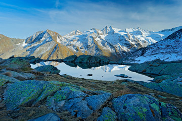 Morning in Italian Alps, mountains with smaůe lake in the rock, hills in the clouds, Alp, Gran Paradiso, Italy. Mountain landscpe with blue sky with white clouds.