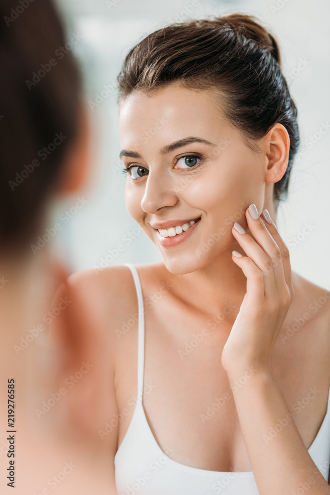 Wall mural beautiful smiling young woman looking at mirror in bathroom