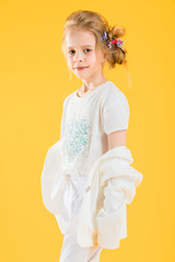 Fototapeta na wymiar A teenage girl in white clothes posing on a yellow background. The girl lowered her jacket to her elbows.