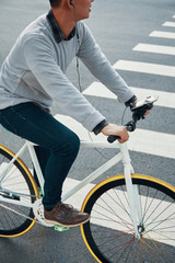 Crop guy in casual outfit listening to music in earphones and looking away while riding bicycle near crosswalk on city road