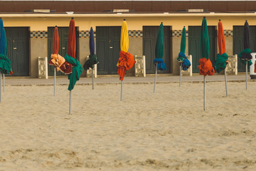 Beach umbrellas on foggy morning in Deauville, fashionable holiday resort in Normandy, France. Beach boxes and folded colorful parasols on the empty beach. Leisure and seaside vacations concept.