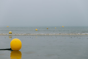 Yellow buoys during low tide on the beach of Deauville in Normandy, France. Beach season and vacation concept. Seascape on a misty morning
