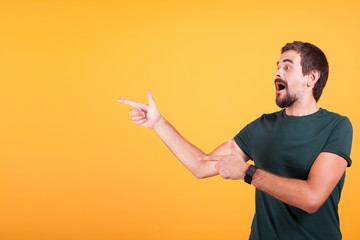 Enthusiasm and expressive man pointing at the copyspace available for your text, promo or advertising. The male is surprised and happy. Orange background