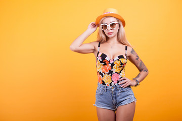 Happy beautiful woman posing in sunglasses and hat over yellow background