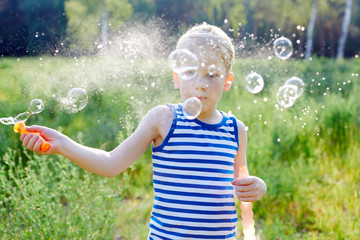Little blond boy makes bubbles soap outside in a park