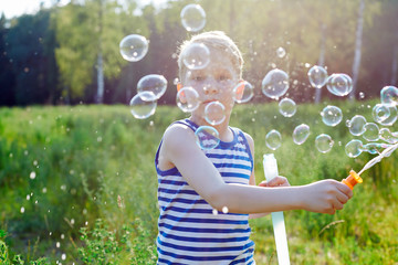 Little blond boy makes bubbles soap outside in a park