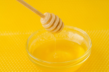 A spoon for honey in a plate with honey on a yellow background