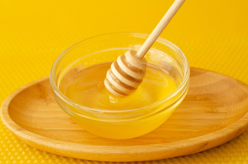 A spoon for honey in a plate with honey on a yellow background