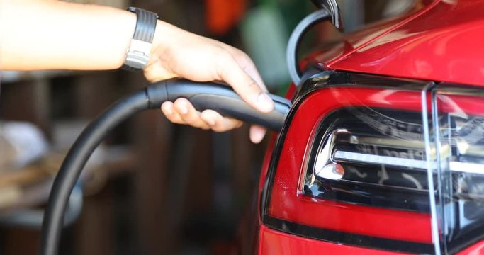 Close up of a red electric car's charge port automaticlaly opening, and being plugged in.