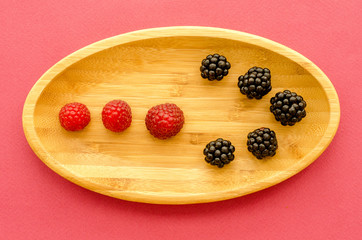 wooden plate with berries on a pink background