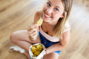 Beautiful young woman eating patatoes while sitting on the floor at home. © nenetus