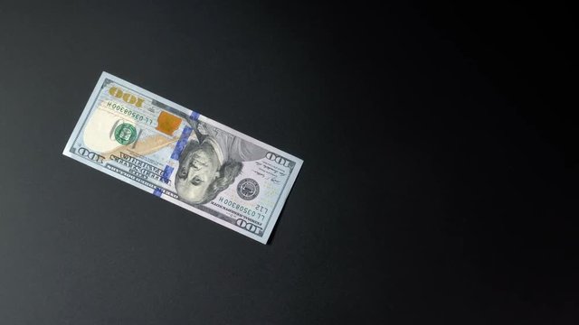 One 100 dollar bill turns on a black background isolated 4k closeup close-up.