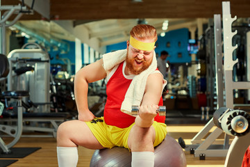 Thick man doing exercises with a barbell in the gym.