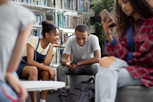 High school students looking at smartphone in a library