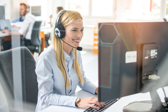 Smiling young female customer service representative with headset in call center office