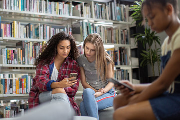 High school students looking at smartphone in a library