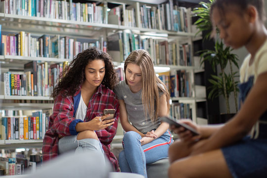 High school students looking at smartphone in a library