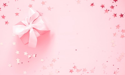 Festive pink background. Gift with satin bow and shining stars on light pink pastel background....
