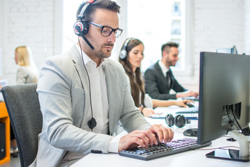 Portrait of a smiling young man with headset using computer in the office