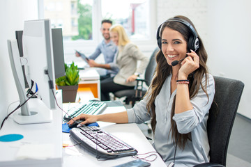 Smiling friendly female call-center agent with headset working on support hotline in the office - Powered by Adobe