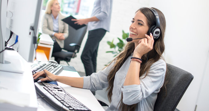 Portrait of beautiful female friendly customer representative with headset smiling during a online telephone conversation with customer.