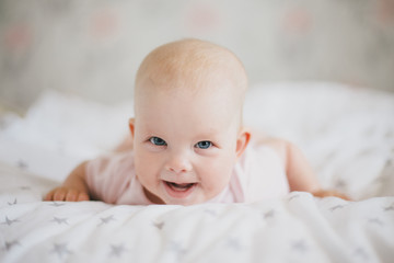 Little cute baby girl wearing pink suit smiling on a bed 