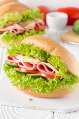 Closed sandwich in bun with ham, cheese, lettuce, tomato, cucumber, red onion. Delicious breakfast, classic lunch