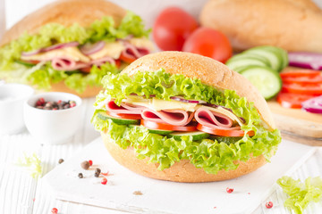 Closed sandwich in bun with ham, cheese, lettuce, tomato, cucumber, red onion. Delicious breakfast, classic lunch
