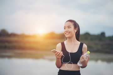 Fitness woman in earphones listening music during her workout and exercise in the park