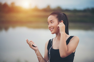 Fitness woman in earphones listening music during her workout and exercise in the park