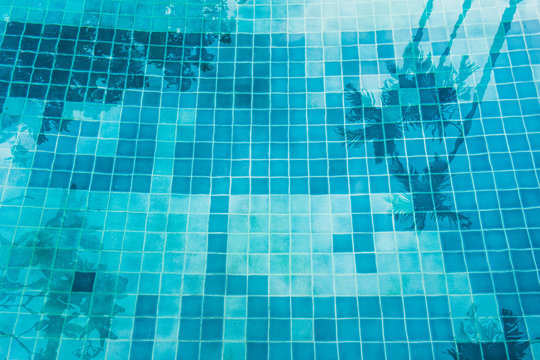 Swimming pool tile at bottom with coconut tree reflect on water.