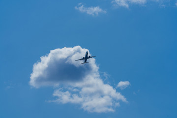 Wide shot photo looking up to the sky of a commercial airline jet flying overhead passing a cloud. Passengers fly all over the world using aviation service companies is big business
