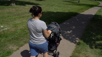 Overhead view young mother walking baby stroller through park on sidewalk on beautiful summer day....