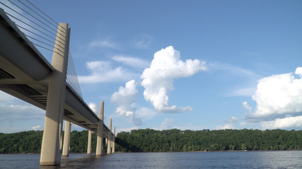 View from boat passing underneath bridge spanning over a river on a clear summer day. Modern construction engineering for road motorway to cross natural borders