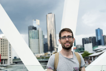 Retrato de hombre joven con gafas frente a paisaje de rascacielos en una gran ciudad sobre un cielo...