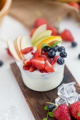 Healthy fruit salad with yoghurt on a wooden plate with ice cubes and fruit as background