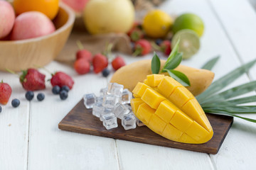 Ripe Mango on a wooden plate with ice cubes and fruit as background