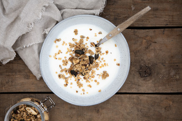 Schüssel mit Joghurt und Granola aus Haferflocken, Nüssen, Leinsamen, Sonnenblumenkernen und Kürbiskernen auf einem alten Holzuntergrund