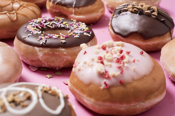 Closeup of Classic chocolate ring donut (doughnut) on a pastel pink background with sprinkles and other donuts scattered around