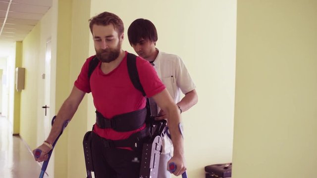 Young disable man walking in the robotic exoskeleton in the rehabilitation clinic.