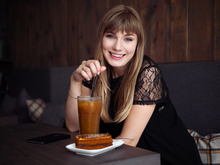 Charming young woman with beautiful smile enjoying orange juice frappe in cozy coffee shop relaxing during free time