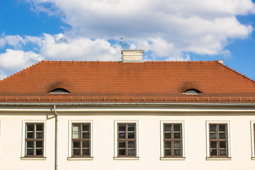 symmetry small european house facade with red shingles roof and windows on blue sky clouds background with empty space for copy or text