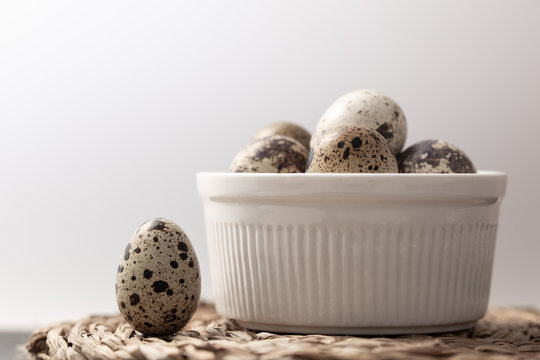Still life with a white bowl of eggs and another egg standing out on a straw mat