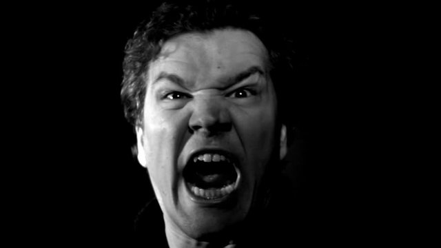 Furious yelling man in slow motion. This guy is so angry he's making an evil screaming rage face. Raging and livid, man moves in close with serious expression.