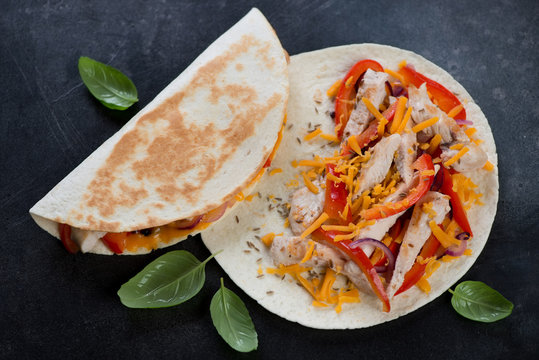 Quesadillas with grilled chicken meat, vegetables and cheddar cheese, high angle view on a dark metal background