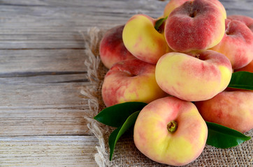 Fresh organic chinese flat peaches with leaves on old wooden background.Saturn donut, Doughnut peach, Paraguayo.Healthy eating or diet concept.Selective focus.