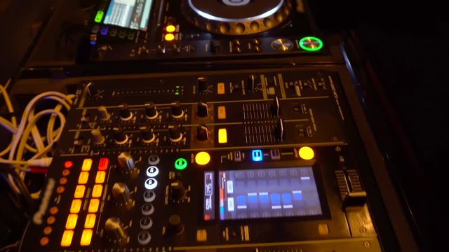 Moving over DJ turntables and mixer with hands playing. Dolly over DJ playing on his equipment, pushing buttons and moving sliders, with CD turntables playing music.