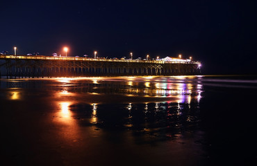 Night view with glowing in the dark illumination at atlantic ocean beach wooden pier and bright lights reflection in the ocean water. South Carolina, Garden City,Myrtle Beach area.
