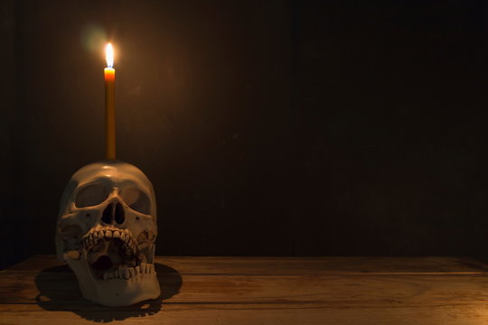 Human skull with candle light on wooden table in the dark background, Decorate for Halloween Theme with copy space.