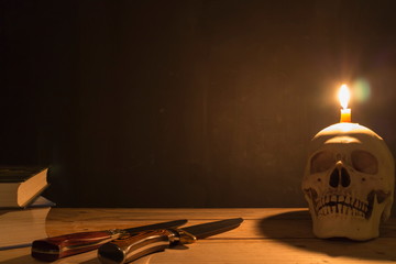 Human skull with candle light, Knife and book on wooden table in the dark background, Decorate for Halloween Theme with copy space.